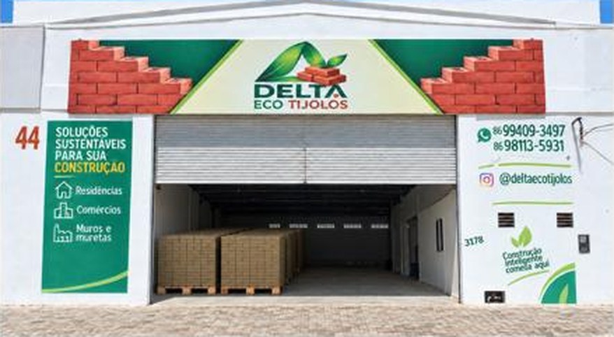 Fachada da fábrica Delta Eco Tijolos em Parnaíba, com o portão aberto e paletes de tijolos ao fundo